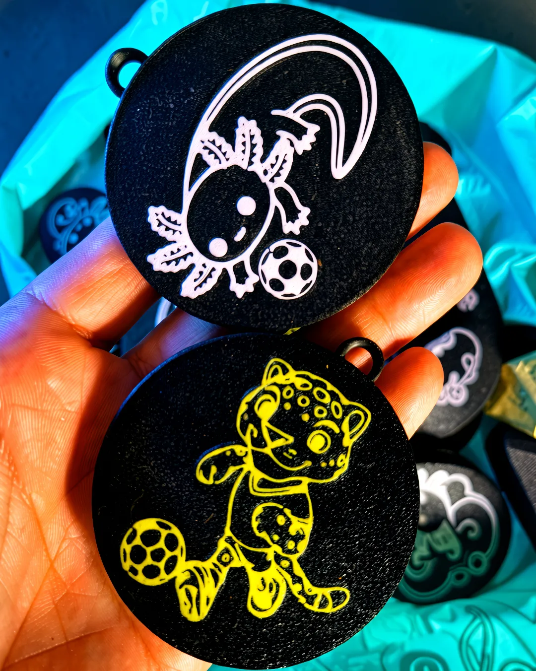 Medallas con ilustraciones en relieve de ajolote y jaguar jugando fútbol